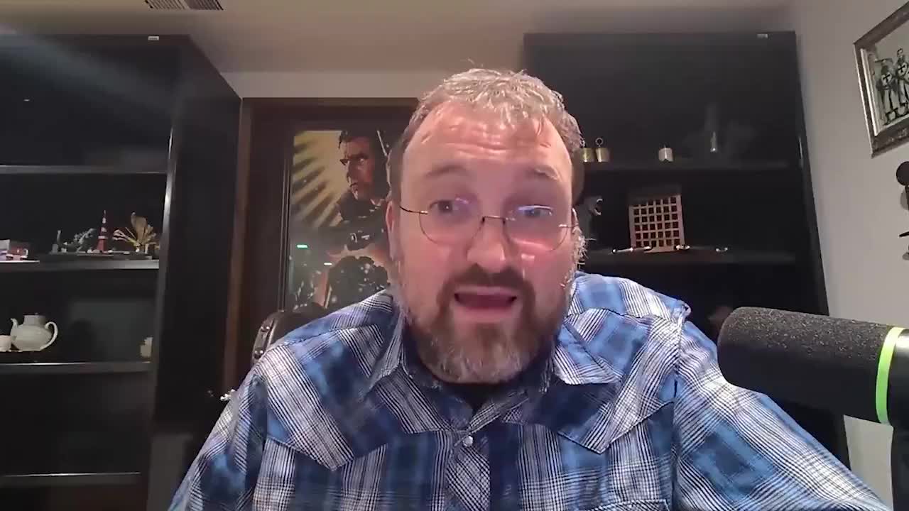 Still from circulating @CoinBureau cut of Charles Hoskinson stream — plaid shirt, glasses, SM7-style mic, shelves behind. Webcam/stream footage. Not Newsmax composite. Not AI.