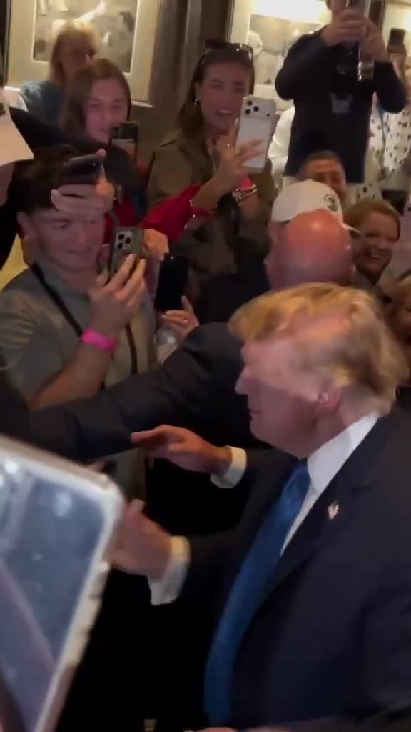 President Donald Trump in the members bar at Trump International Golf Links and Hotel, Doonbeg, County Clare, Saturday 12 September 2026 evening. Phone still. He is in a dark suit and blue tie, right hand out, crowd with phones. Real event still. Not AI.